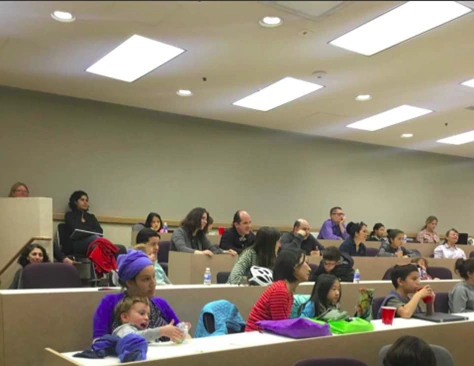 Children and adults attending a public science lecture in a tiered classroom.