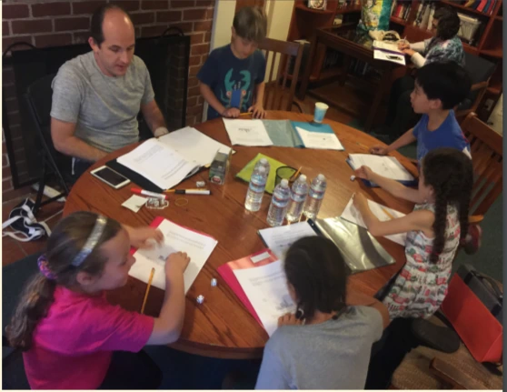 Children and an instructor working with notebooks around a table during an earlier program.