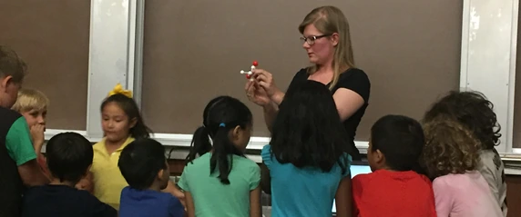 An educator shows a small molecular model to children gathered around her.